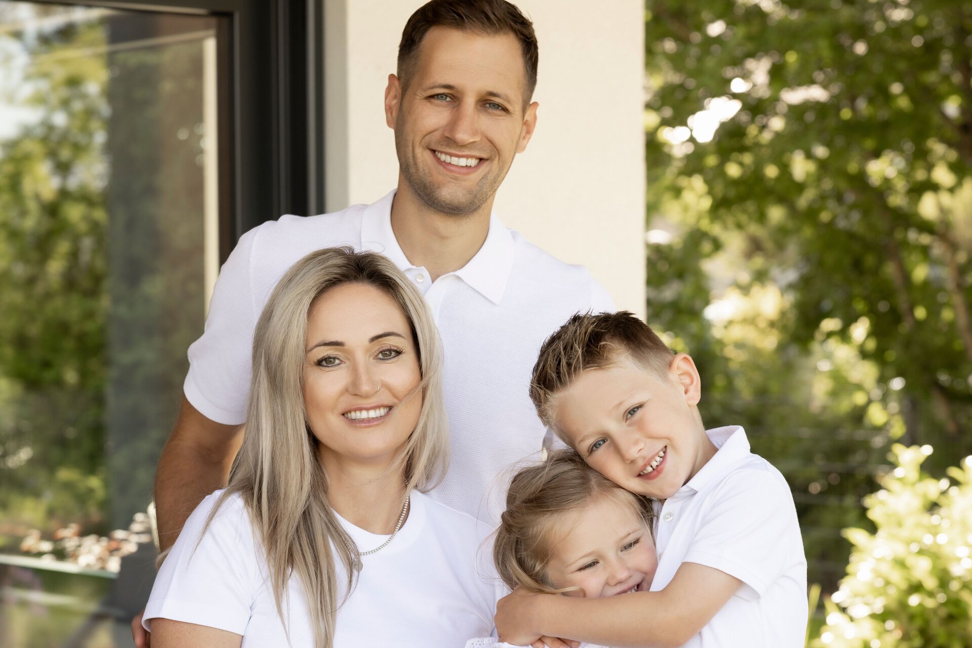 Glückliche Familie in weißer Kleidung sitzt und steht gemeinsam auf der Terrasse eines modernen FingerHaus.