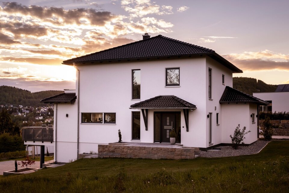 Modernes FingerHaus mit Walmdach und überdachtem Eingangsbereich, malerisch in Szene gesetzt bei Sonnenuntergang mit Blick auf die umliegende Landschaft.