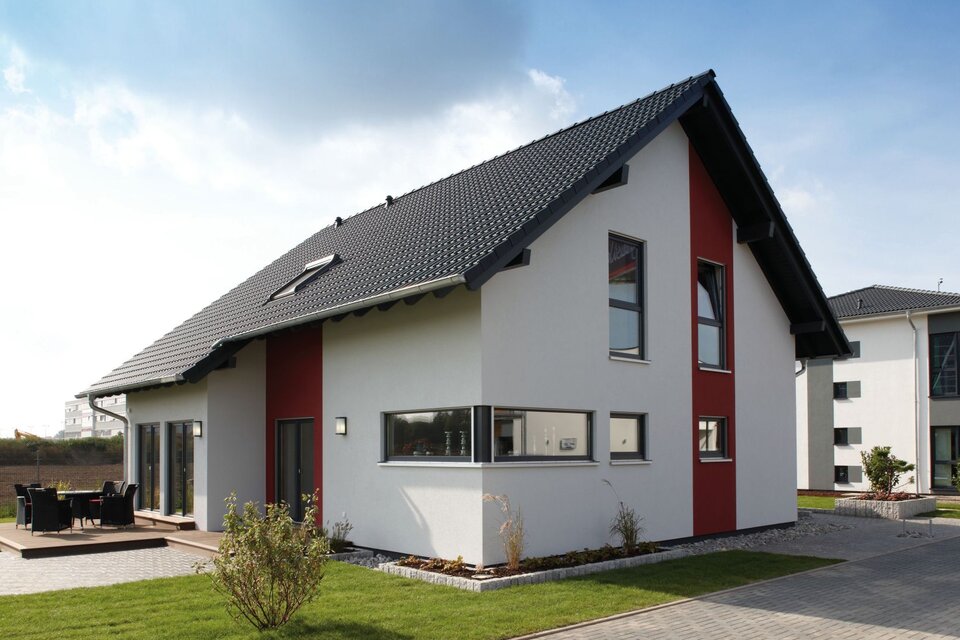 Modernes Musterhaus VIO 400 in Köln mit Satteldach, weißer Fassade und roten Akzenten, umgeben von Terrasse und Garten.