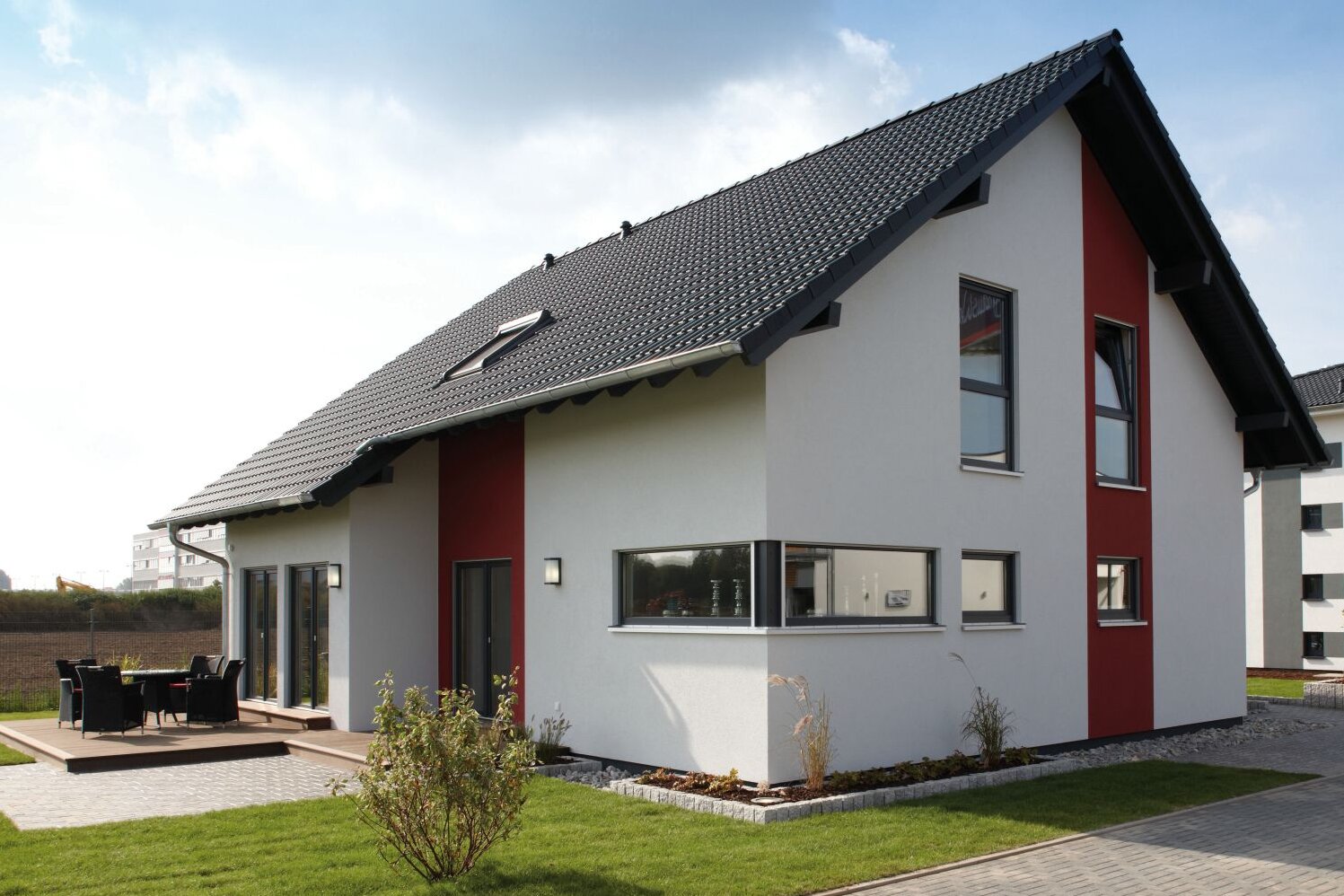 Modernes Musterhaus VIO 400 in Köln mit Satteldach, weißer Fassade und roten Akzenten, umgeben von Terrasse und Garten.
