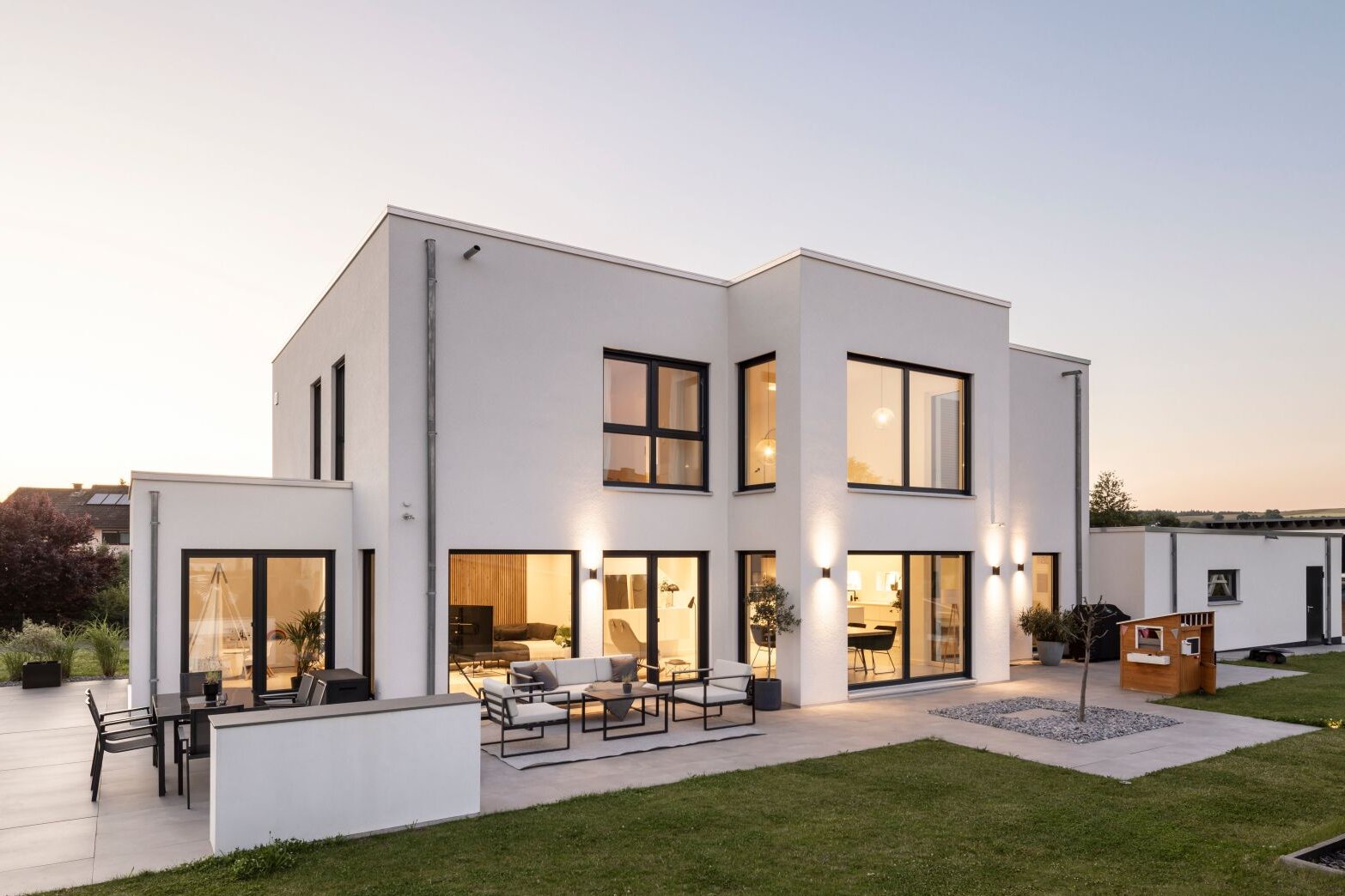 Modernes zweigeschossiges FingerHaus mit klarer, kubischer Architektur, großen Fensterflächen und stilvoll beleuchteter Terrasse in der Abenddämmerung.