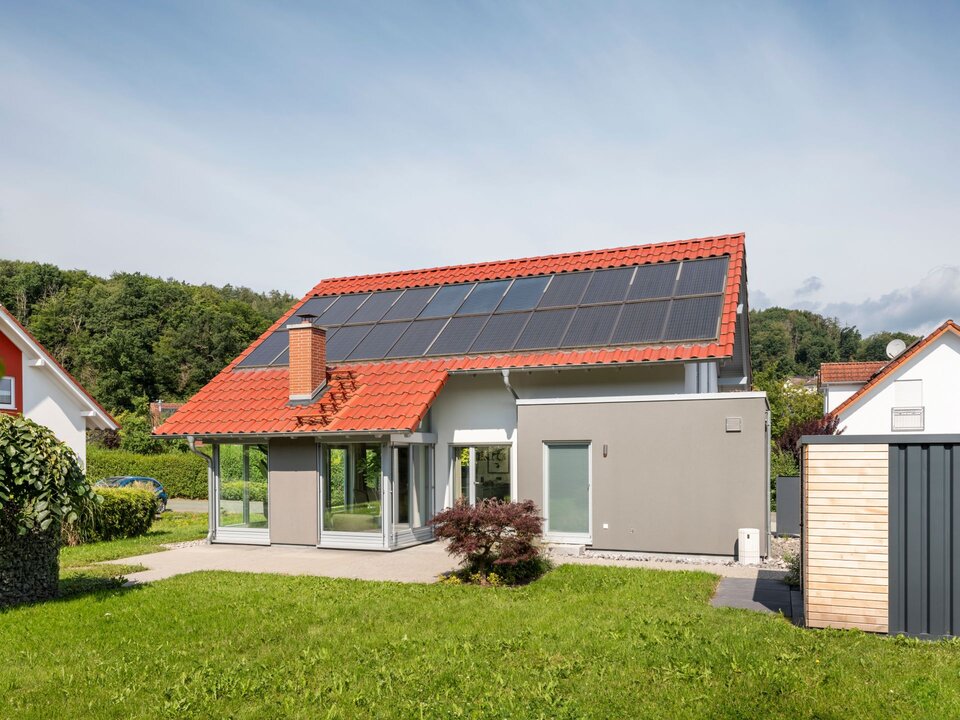 Frei geplantes Musterhaus in Marburg mit rotem Satteldach, Solar-Modulen und großer Glasfassade zum Garten.
