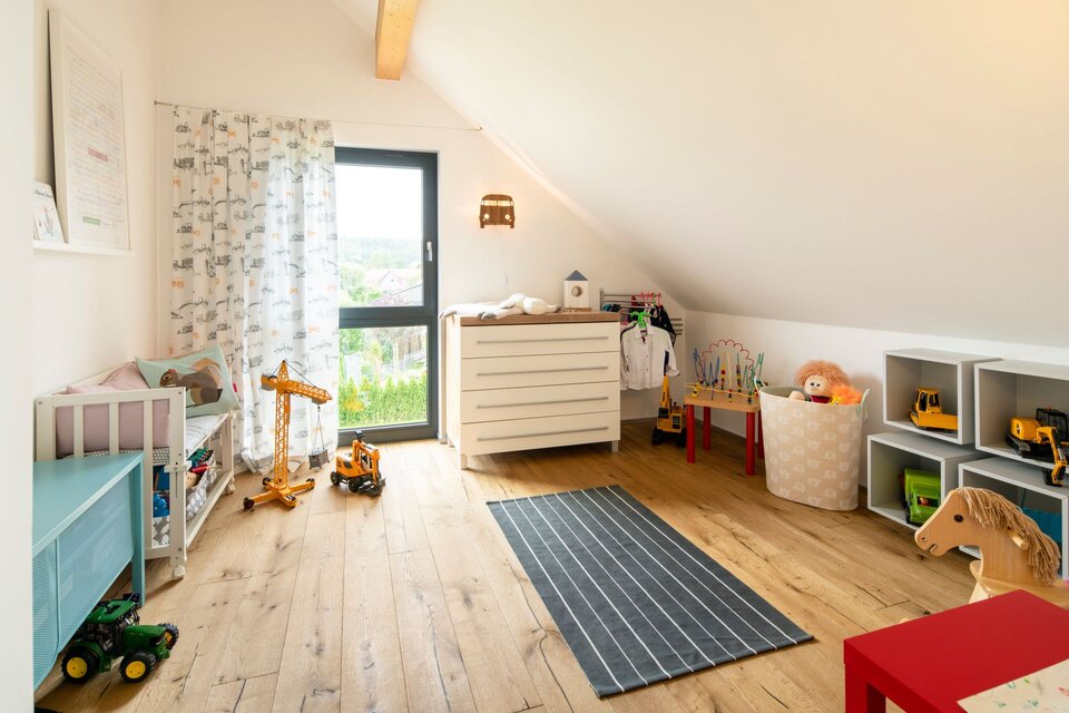Geräumiges Kinderzimmer unter dem Dach mit Dachschräge, Spielbereich und großem Fenster.