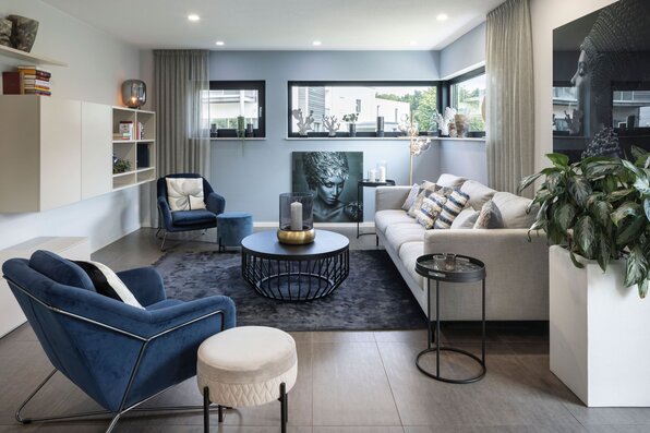 Modernes Wohnzimmer im Musterhaus VIO Köln mit eleganter Sofalandschaft, blauen Akzenten und stilvollen Dekoelementen.