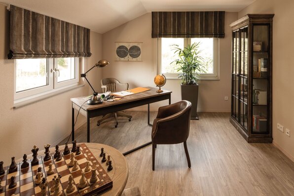 Modernes Arbeitszimmer im FingerHaus SENTO 500 Musterhaus Frankenberg mit Schreibtisch, Bücherregal, Pflanzen und gemütlichem Ambiente unter Dachschrägen.