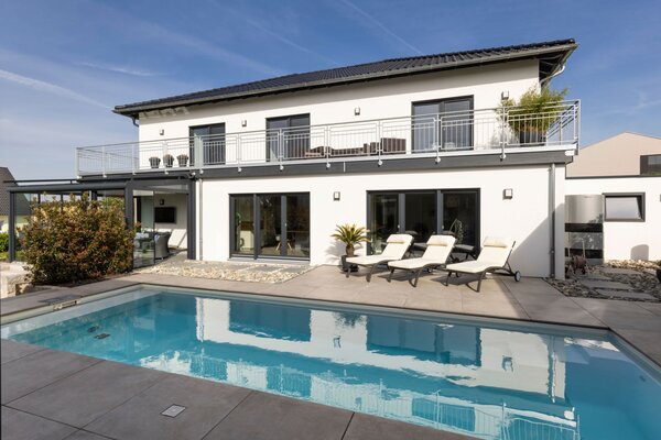 Modernes zweigeschossiges FingerHaus mit großem Pool im Garten, Sonnenterrasse und Balkon bei strahlendem Wetter.