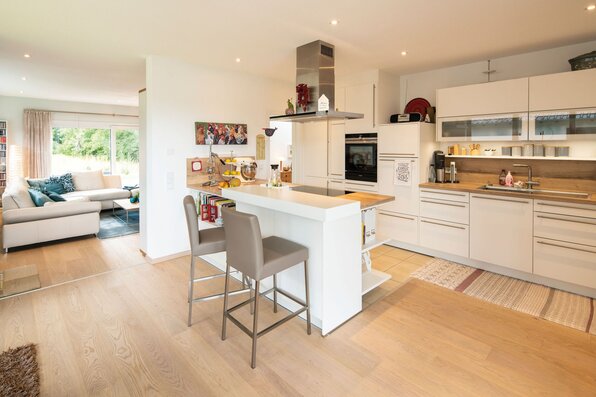 Offene, helle Küche mit Kochinsel, modernen Einbaumöbeln und Blick ins Wohnzimmer in einem FingerHaus.