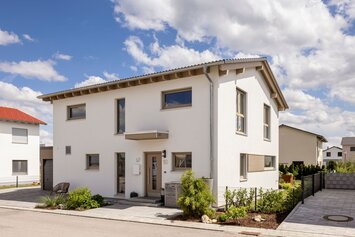 Zweigeschossiges Einfamilienhaus mit Satteldach, heller Putzfassade und überdachtem Eingangsbereich in einem Neubaugebiet