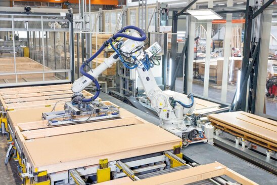 Industrieroboter in der FingerHaus Fertigung montiert präzise Holzrahmen-Elemente für ein Fertighaus auf einer modernen Produktionslinie.