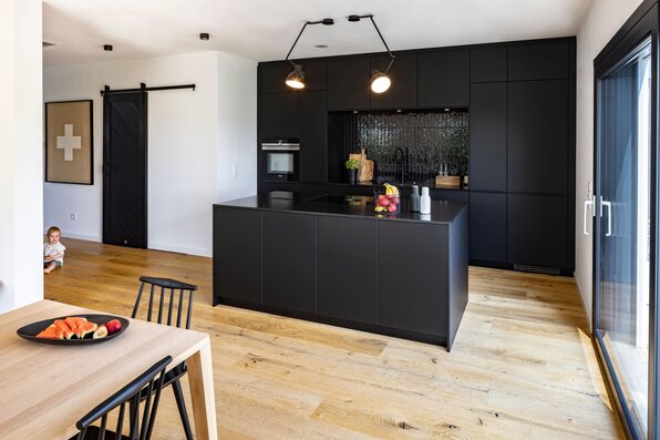 Frei geplante moderne Küche im FingerHaus mit schwarzer Kücheninsel, Holzfußboden und großem Fenster.