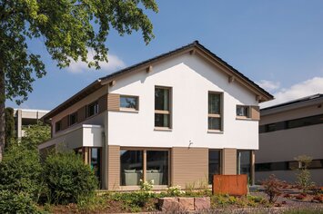 Außenansicht des Musterhauses MEDLEY in Fellbach mit moderner Fassadengestaltung aus Weißputz und Holz-Elementen im Erdgeschoss.