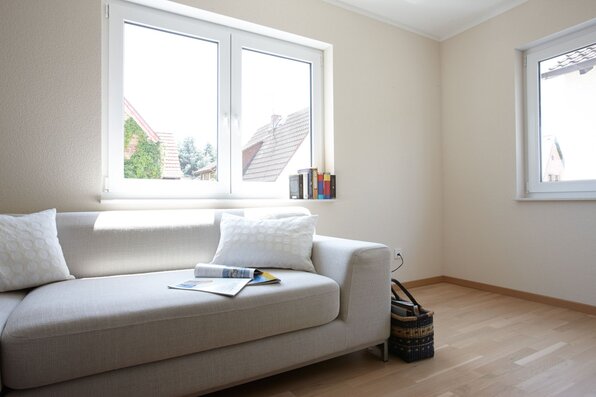 Helles Wohnzimmer mit einem modernen Sofa, Holzboden und großen Fenstern in einem frei geplanten FingerHaus.