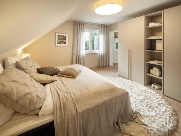 Gemütliches Schlafzimmer im Musterhaus NEO in Wuppertal mit großem Doppelbett, modernem Kleiderschrank und hellem Teppich.