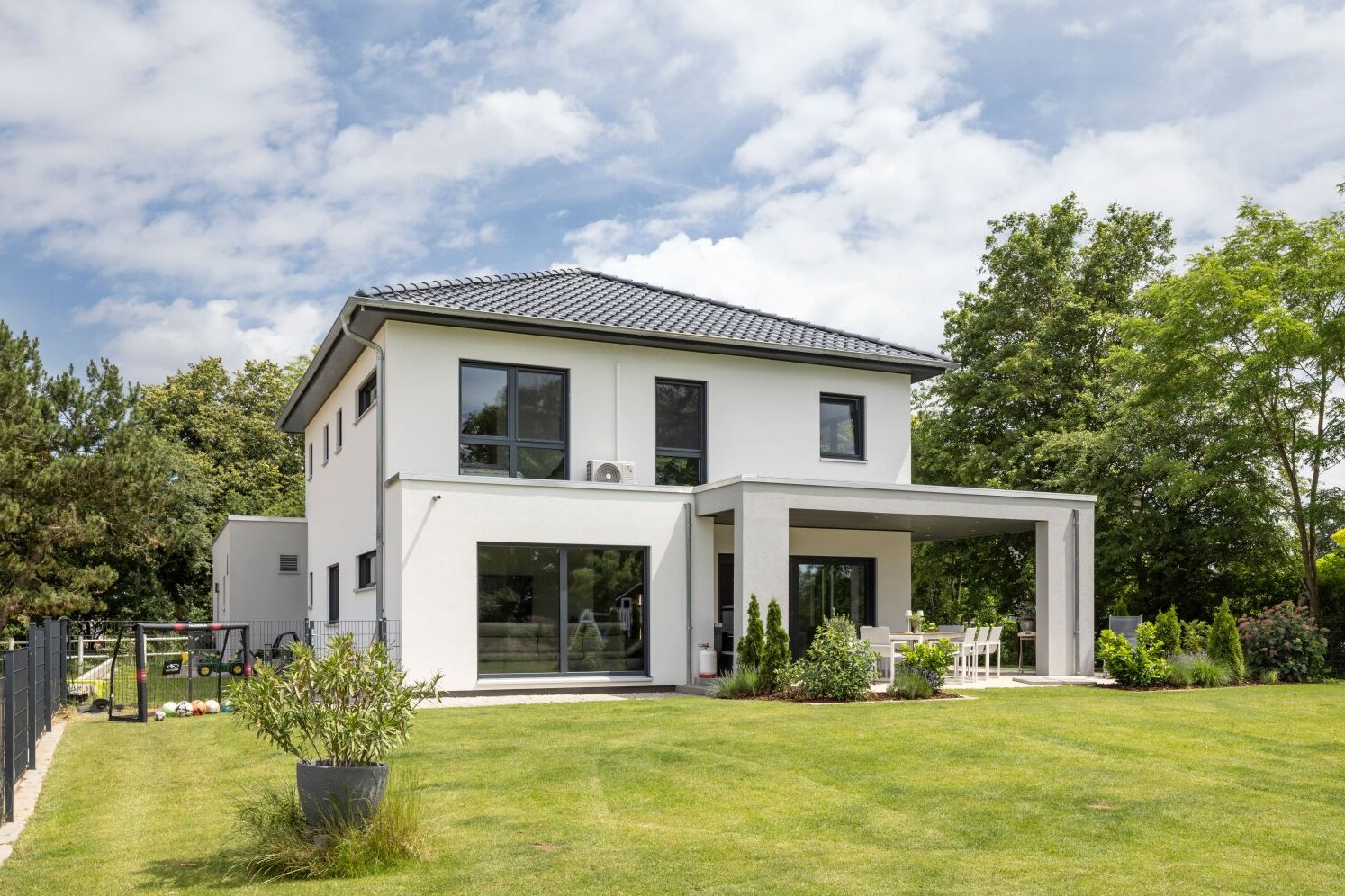 Modernes FingerHaus mit weißer Fassade, Flachdach-Elementen, überdachter Terrasse und gepflegtem Garten.