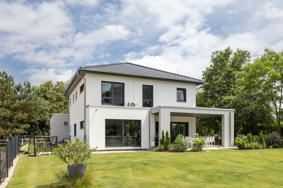 Modernes FingerHaus mit weißer Fassade, Flachdach-Elementen, überdachter Terrasse und gepflegtem Garten.