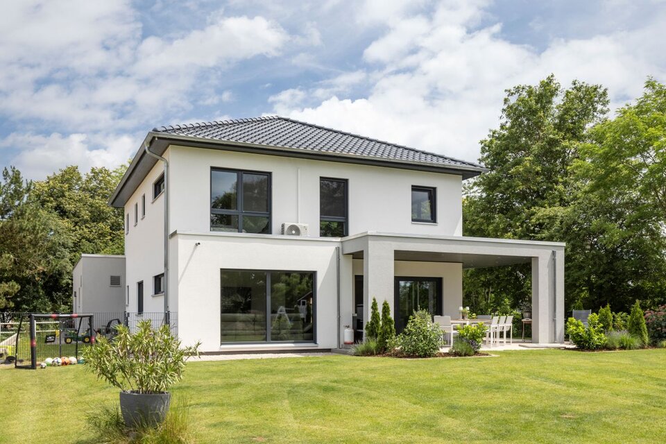 Modernes FingerHaus mit weißer Fassade, Flachdach-Elementen, überdachter Terrasse und gepflegtem Garten.
