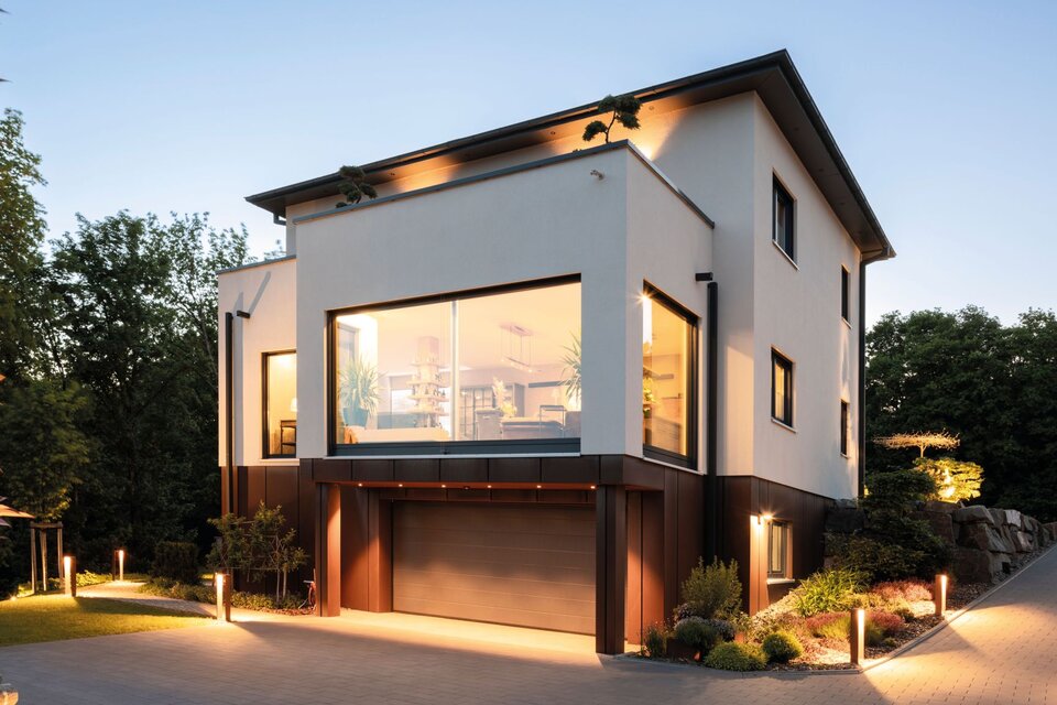 Modernes frei geplantes FingerHaus mit großen Fensterfronten und Garage im Abendlicht.