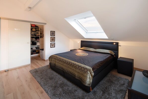 Gemütliches Schlafzimmer unterm Dach in einem FingerHaus-Haus mit Dachflächenfenster, Doppelbett und offener Ankleide.