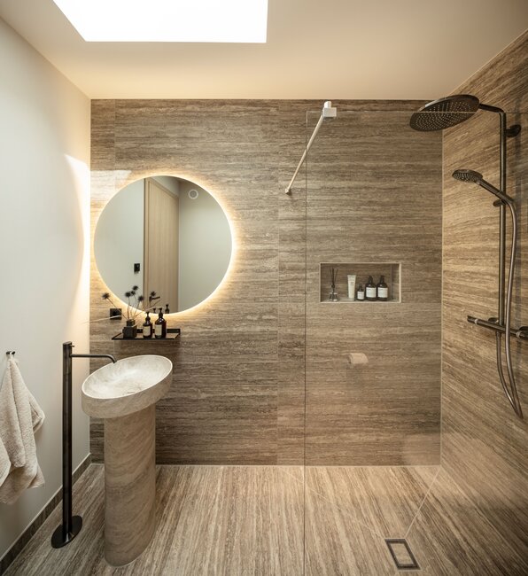 Duschbad im FingerHaus Musterhaus NIVO in Frankenberg mit bodengleicher Dusche, Standwaschbecken und rundem beleuchtetem Spiegel.