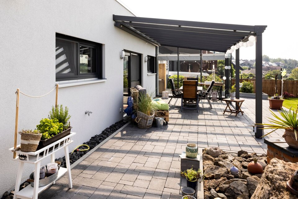 Gepflasterte Terrasse eines modernen Flachdachhauses mit überdachter Sitzgruppe, Pflanzen und dekorativen Elementen