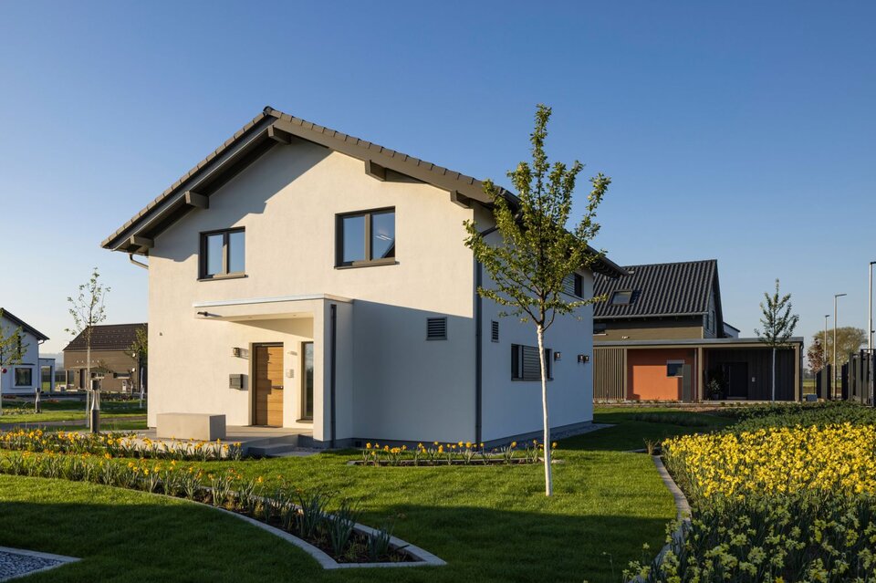 FingerHaus ARTIS 400 Musterhaus im Schwarzwald mit Satteldach, weißer Fassade, modernem Eingangsbereich und gepflegtem Garten mit Blumenbeeten.