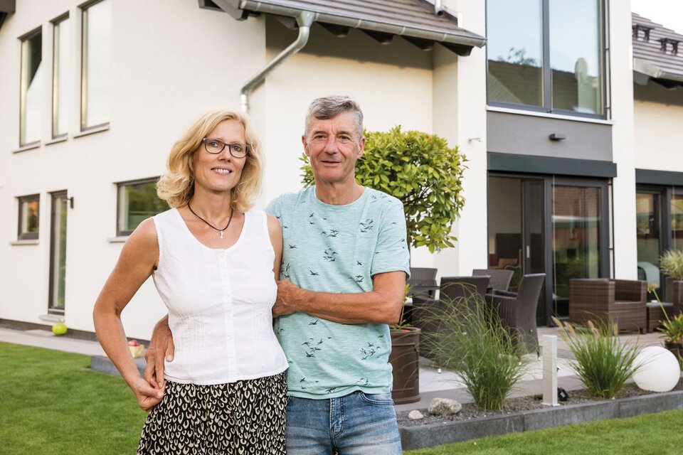 Zwei Personen stehen lächelnd im Garten vor einem frei geplanten FingerHaus mit großer Terrasse und moderner Fassadengestaltung.