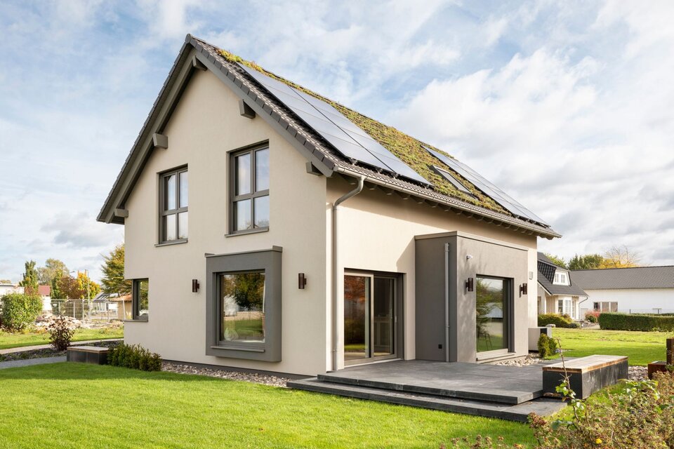 Rückansicht des Musterhauses JUNO 300 in Mülheim-Kärlich mit begrüntem Dach, Solarpaneelen und Terrasse.