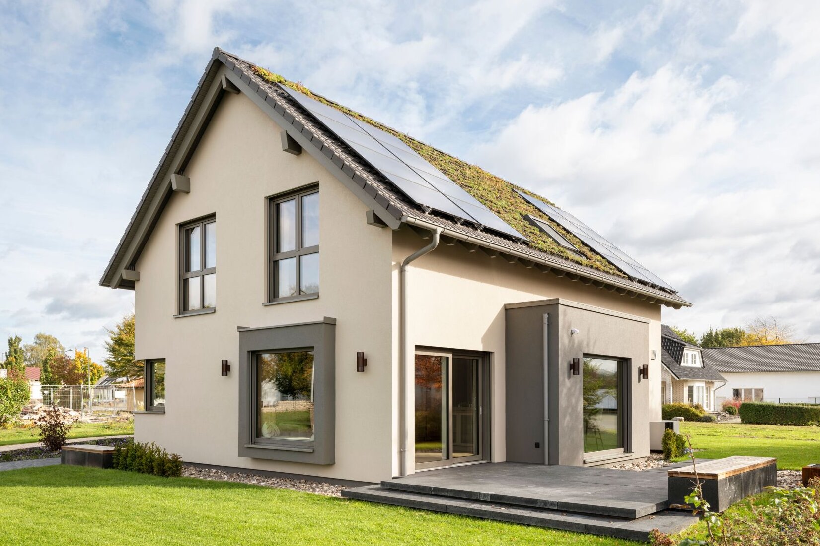 Rückansicht des Musterhauses JUNO 300 in Mülheim-Kärlich mit begrüntem Dach, Solarpaneelen und Terrasse.