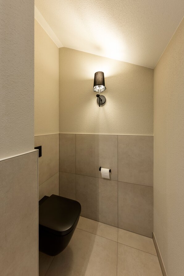 Kompaktes Gäste-WC im FingerHaus ARTIS 300 Musterhaus Würzburg mit moderner Wandlampe und dunkler Keramik.