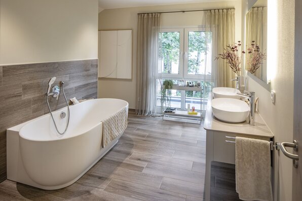 Modernes Badezimmer im MEDLEY Musterhaus Mannheim mit freistehender Badewanne, Doppelwaschbecken und großem Fenster.