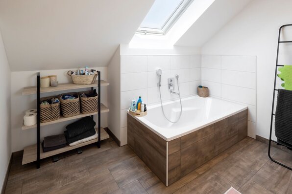 Badezimmer im Obergeschoss des SENTO 403 mit Badewanne unter Dachschräge, Dachfenster und offenem Regal