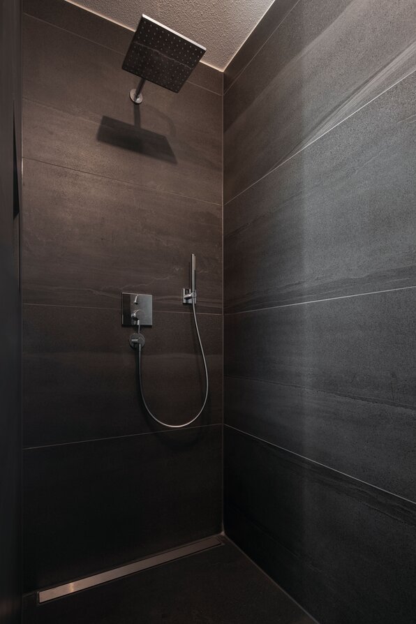 Moderne begehbare Dusche im Musterhaus MEDLEY 300 B in Frankenberg mit dunklen großformatigen Fliesen und Regendusche.