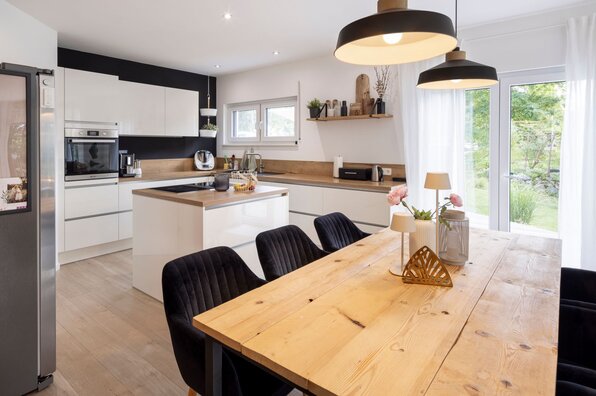 Moderne Küche mit Esstisch in einem frei geplanten FingerHaus, ausgestattet mit heller Einrichtung, Holzarbeitsplatten und großen Fenstern zum Garten.