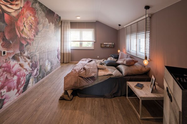 Schlafzimmer im FingerHaus SENTO 500 Musterhaus in Frankenberg mit gemütlichem Doppelbett, Holzfußboden und auffälliger Blumenmuster-Wandgestaltung.