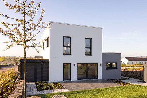Musterhaus TALO in Fulda mit moderner Kubusarchitektur, großem Garten und klaren Linien bei Sonnenuntergang.