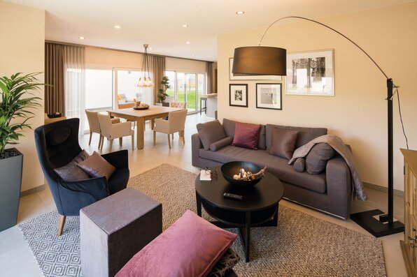 Wohnzimmer im FingerHaus NEO Musterhaus Günzburg mit gemütlicher Sofaecke, eleganter Stehlampe und Blick in den Essbereich.