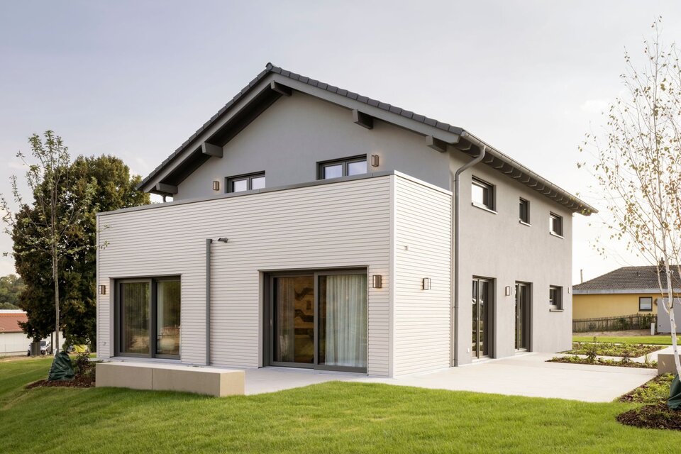 Außenansicht des FingerHaus ARTIS 300 Musterhauses Würzburg mit grauer Fassade, Flachdachanbau und großen Fensterfronten.