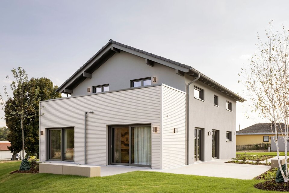 Außenansicht des FingerHaus ARTIS 300 Musterhauses Würzburg mit grauer Fassade, Flachdachanbau und großen Fensterfronten.