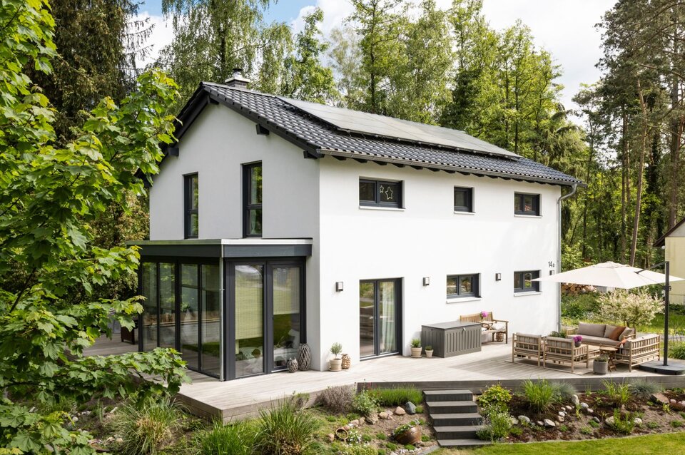 Frei geplantes FingerHaus mit Satteldach, moderner Terrasse und Wintergarten, eingebettet in eine grüne Gartenlandschaft.