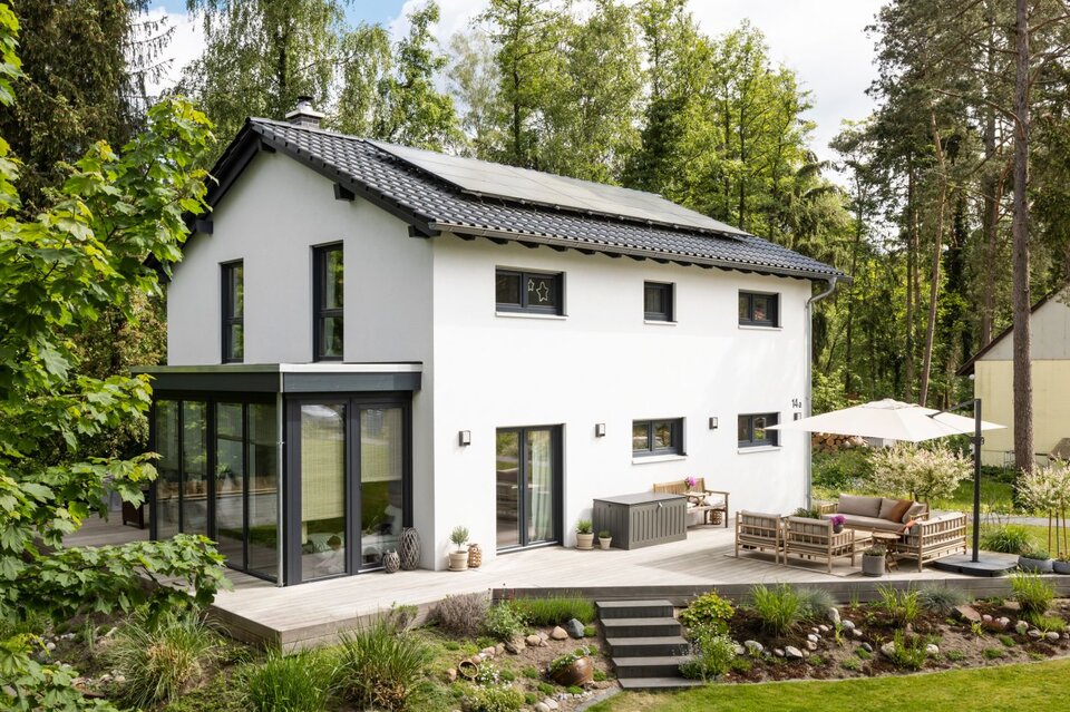 Frei geplantes FingerHaus mit Satteldach, moderner Terrasse und Wintergarten, eingebettet in eine grüne Gartenlandschaft.