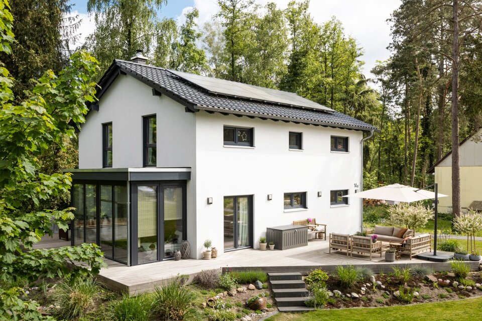 Frei geplantes FingerHaus mit Satteldach, moderner Terrasse und Wintergarten, eingebettet in eine grüne Gartenlandschaft.