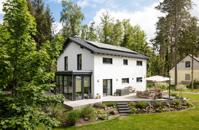 Frei geplantes FingerHaus mit Satteldach, moderner Terrasse und Wintergarten, eingebettet in eine grüne Gartenlandschaft.
