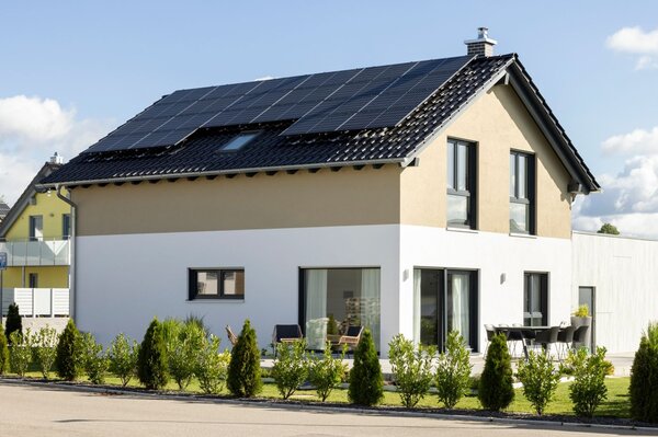 Einfamilienhaus des Hausmodells NEO 211 von FingerHaus mit Satteldach und Photovoltaikanlage bei Tageslicht, helle Putzfassade mit zweifarbiger Gestaltung, bodentiefe Fenster, Terrasse mit Sitzmöbeln und gepflegte Gartenbepflanzung.