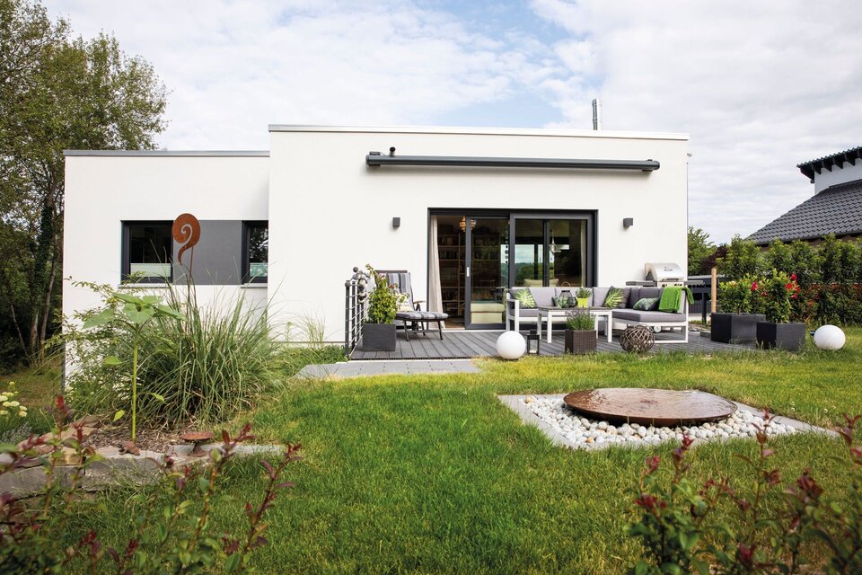 Moderner Bungalow von FingerHaus mit weißer Fassade, großer Terrasse mit Lounge-Möbeln, gepflegtem Garten und dekorativen Elementen.