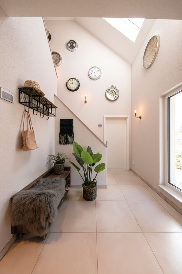 FingerHaus JUNO 402 Musterhaus Frankenberg – moderner Eingangsflur mit Treppe, großer Fensterfront und dekorativen Wanduhr-Elementen