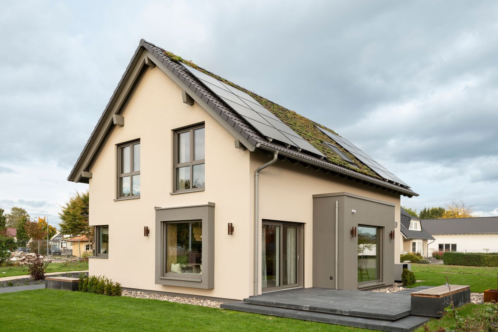 Moderne Außenansicht des Musterhauses JUNO 300 in Mülheim-Kärlich mit Gründach, Photovoltaikanlage und großen Fenstern.