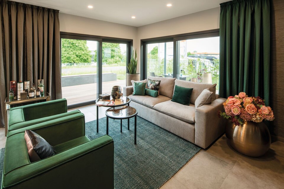 Elegantes Wohnzimmer im FingerHaus MAXIM mit grünen Akzenten, gemütlichem Sofa und großen Fensterfronten, Musterhaus Gießen.