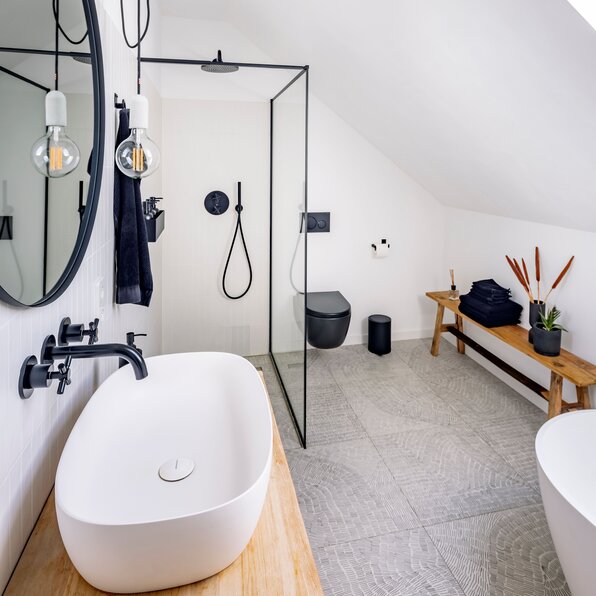 Modernes Bad im Dachgeschoss eines FingerHaus-Hauses mit freistehender Badewanne, ebenerdiger Dusche mit schwarzem Rahmen und hellen Naturmaterialien.