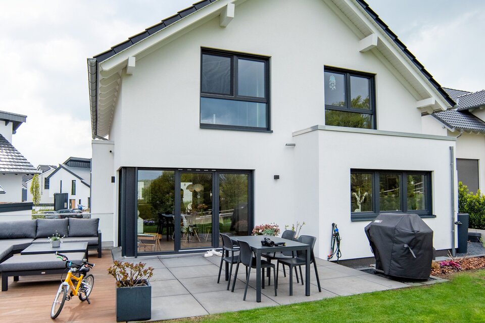 Rückansicht eines frei geplanten FingerHaus mit moderner Terrasse, Gartenmöbeln und direktem Zugang ins Haus.