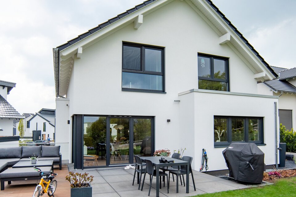 Rückansicht eines frei geplanten FingerHaus mit moderner Terrasse, Gartenmöbeln und direktem Zugang ins Haus.